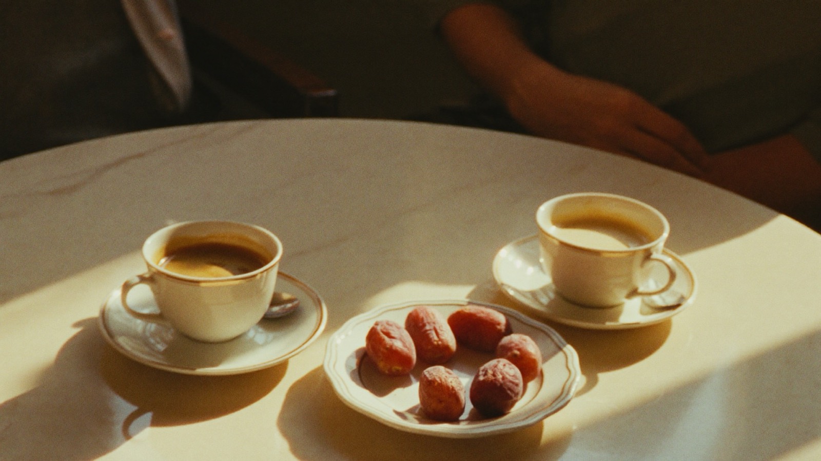 Two cups of Arabic coffee and a plate of dates on a sunlit marble table, set for a conversation